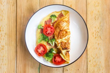 Jambonlu omlet, brokoli ve domates karışımı ahşap bir masada.