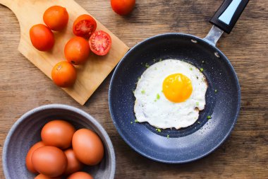 Tavada yumurta, domates ve ahşap bir masada malzemeler.