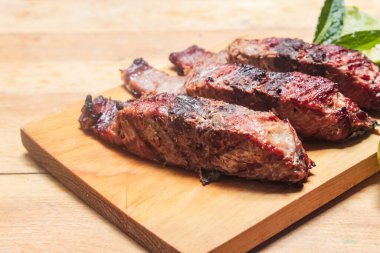 Tahta bir masanın üzerinde kepçe ve çatal ve kaşıkla ızgara balık dilimleri ve limon.