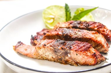 Izgara balık dilimleri ve yanında çatal ve kaşıkla bir tabakta limon.