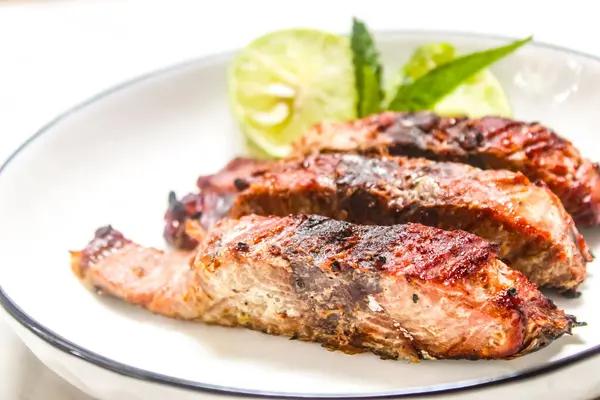 Izgara balık dilimleri ve yanında çatal ve kaşıkla bir tabakta limon.