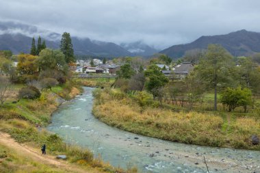 Japon Alpleri 'nin arka planda olduğu Hakuba Köyü' nün güzel manzarası ve sonbaharda içinden akan temiz bir dere, Oide Park, Nagano Bölgesi, Japonya manzarası 