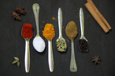Siyah arka plan üzerine kaşık içinde çeşitli baharatlar. Üstten Görünüm