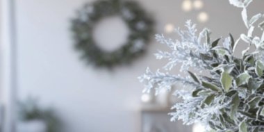 A serene winter decoration with frosted foliage and a festive wreath in the background. clipart