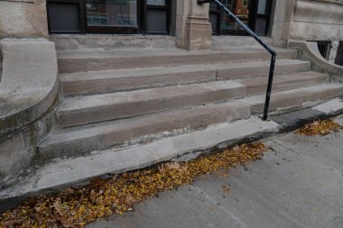 Bir apartmanın dışındaki kaygan merdivenler çatlamış ve ufalanmış, sonbahar yaprakları, yatay görünüm.