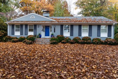 Small suburban ranch house with roof and yard covered in leaf litter, needing yard maintenance, horizontal aspect