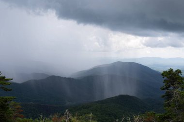 Sheets of rain falling thickly on a mountain vista obscuring parts of the distance, rainy weather event from a cloudburst, horizontal aspect