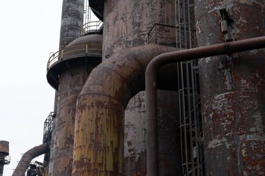 Terk edilmiş bir çelik fabrikasının patlayıcı fırınları ve ağır metal mimarisi kışın gri gökyüzüne karşı, yatay olarak