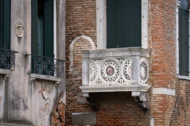 Venedik 'te camları ve oyulmuş taş balkonu olan bir cephe. Eski bir Venedik binasının oyulmuş taş balkonları..
