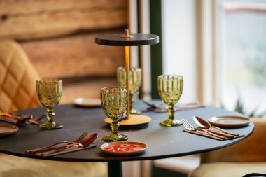 Yuvarlak servis masası misafirler için hazır. Boş tabak, bardak, çatal ve peçeteyle dekore edilmiş yuvarlak masa. Zarif bir yemek masası..