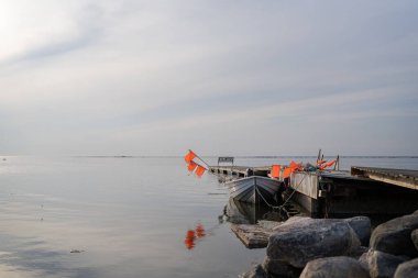 İskelenin yanında ağ bayraklı küçük bir balıkçı teknesi. Akşamları deniz kıyısında balıkçı teknesi ve tekne. Denizin üzerinde gün batımı, ahşap bir iskele ve bir bankla..