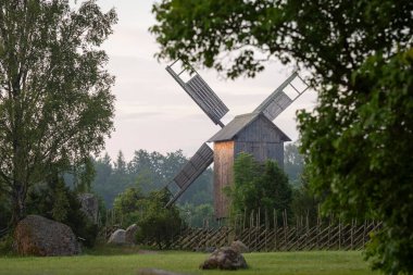 Güneşin doğuşunda eski yel değirmeniyle yaz manzarası. Orman açıklığında antik ahşap yel değirmeni. Yaz kırsalında güneş doğarken.