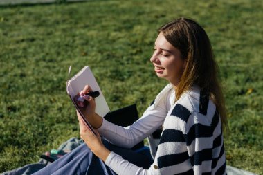 Öğrenci kız yazın dışarıda çalışıyor. Holliday 'de yeşil çimlerin üzerinde dizüstü bilgisayar kullanıyor ve not alıyor.