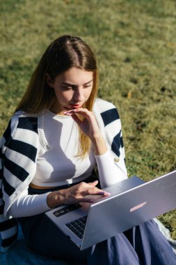 Öğrenci kız yazın dışarıda çalışıyor. Holliday 'de yeşil çimlerin üzerinde dizüstü bilgisayar kullanıyor ve not alıyor.