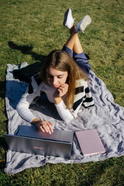 Öğrenci kız yazın dışarıda çalışıyor. Holliday 'de yeşil çimlerin üzerinde dizüstü bilgisayar kullanıyor ve not alıyor.