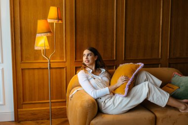 Harika bir atmosferi ve sarı lambası olan rahat bir odada kanepede uzanmış genç bir kız. Yüksek kalite fotoğraf