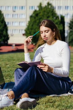 Öğrenci kız yazın dışarıda çalışıyor. Holliday 'de yeşil çimlerin üzerinde dizüstü bilgisayar kullanıyor ve not alıyor.