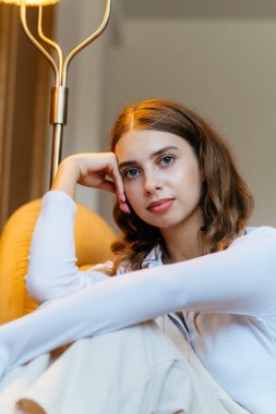 Beyaz elbiseli, sarı ışıklı kanepe yastıklı, rahat, kaliteli bir odada genç bir kız. Yüksek kalite fotoğraf