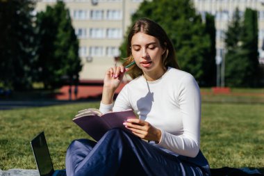 Öğrenci kız yazın dışarıda çalışıyor. Holliday 'de yeşil çimlerin üzerinde dizüstü bilgisayar kullanıyor ve not alıyor.