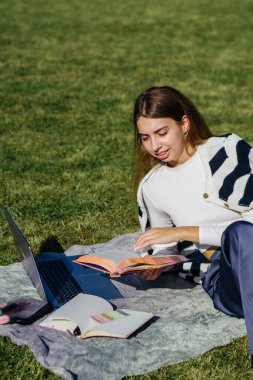 Öğrenci kız yazın dışarıda çalışıyor. Holliday 'de yeşil çimlerin üzerinde dizüstü bilgisayar kullanıyor ve not alıyor.