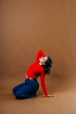 Kalın kırmızı bluzlu ve geniş paçalı kot pantolonlu şık bir genç kadın, dinamik ve sanatsal bir poz veriyor. Yüksek kalite fotoğraf