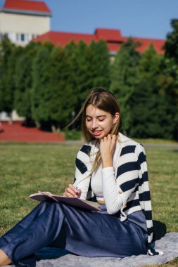 Öğrenci kız yazın dışarıda çalışıyor. Holliday 'de yeşil çimlerin üzerinde dizüstü bilgisayar kullanıyor ve not alıyor.