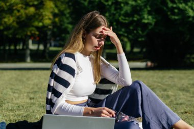 Öğrenci kız yazın dışarıda çalışıyor. Holliday 'de yeşil çimlerin üzerinde dizüstü bilgisayar kullanıyor ve not alıyor.