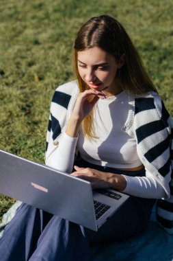 Öğrenci kız yazın dışarıda çalışıyor. Holliday 'de yeşil çimlerin üzerinde dizüstü bilgisayar kullanıyor ve not alıyor.