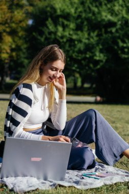 Öğrenci kız yazın dışarıda çalışıyor. Holliday 'de yeşil çimlerin üzerinde dizüstü bilgisayar kullanıyor ve not alıyor.