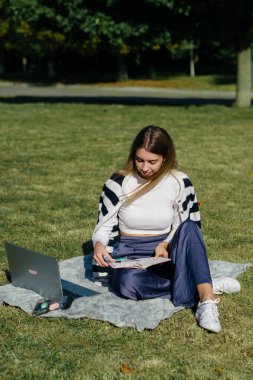 Öğrenci kız yazın dışarıda çalışıyor. Holliday 'de yeşil çimlerin üzerinde dizüstü bilgisayar kullanıyor ve not alıyor.
