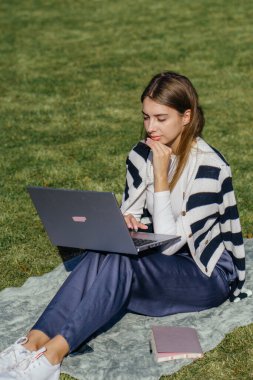 Öğrenci kız yazın dışarıda çalışıyor. Holliday 'de yeşil çimlerin üzerinde dizüstü bilgisayar kullanıyor ve not alıyor.