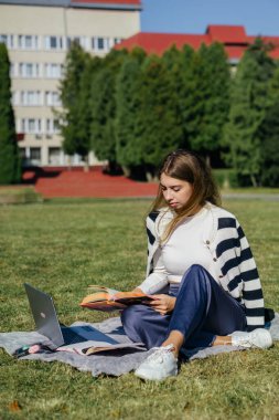 Öğrenci kız yazın dışarıda çalışıyor. Holliday 'de yeşil çimlerin üzerinde dizüstü bilgisayar kullanıyor ve not alıyor.