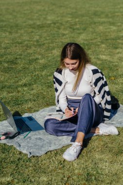 Öğrenci kız yazın dışarıda çalışıyor. Holliday 'de yeşil çimlerin üzerinde dizüstü bilgisayar kullanıyor ve not alıyor.