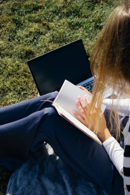 Öğrenci kız yazın dışarıda çalışıyor. Holliday 'de yeşil çimlerin üzerinde dizüstü bilgisayar kullanıyor ve not alıyor.