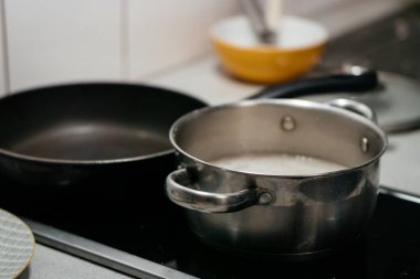 Mutfak malzemelerinin ve çatalların bulanık arkaplanına sahip, paslanmaz çelik bir tencerede yemek pişirirken çekilmiş yakın plan bir fotoğraf. Sıcak bir ev yemeği anı yakalıyor. Yüksek kalite fotoğraf