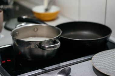 Mutfak malzemelerinin ve çatalların bulanık arkaplanına sahip, paslanmaz çelik bir tencerede yemek pişirirken çekilmiş yakın plan bir fotoğraf. Sıcak bir ev yemeği anı yakalıyor. Yüksek kalite fotoğraf