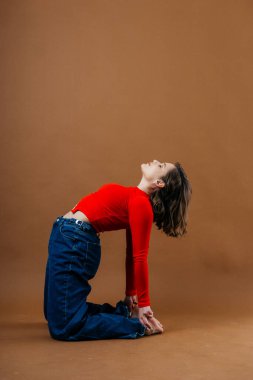 Kalın kırmızı bluzlu ve geniş paçalı kot pantolonlu şık bir genç kadın, dinamik ve sanatsal bir poz veriyor. Yüksek kalite fotoğraf