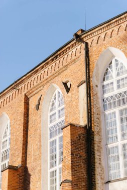 Büyük kemerli pencereli, parlak mavi gökyüzü altında karmaşık mimari detaylar barındıran tarihi kırmızı tuğla bir binanın yakın çekimi. Estonya Tartu Üniversitesi. Yüksek kaliteli fotoğraf Estonya
