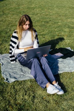 Öğrenci kız yazın dışarıda çalışıyor. Holliday 'de yeşil çimlerin üzerinde dizüstü bilgisayar kullanıyor ve not alıyor.