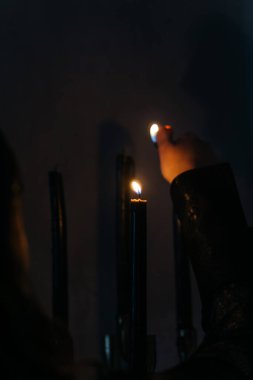 Karanlık odada mum yakmak romantik atmosfer ateşler. Yüksek kaliteli bir fotoğraf. Karamsar ve atmosferik bir sahne. Siyah mum yakan, gizemi, ritüeli ve loş bir sembolizmi çağrıştıran bir kişi.