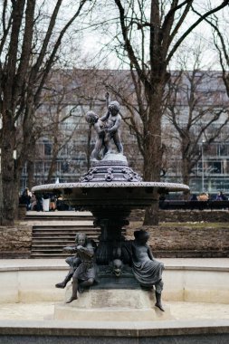 Yapraksız ağaçlar ve klasik mimari ile çevrili huzurlu bir şehir parkında, karmaşık heykellerle süslenmiş güzel, tarihi bir çeşme duruyor. Yüksek kalite fotoğraf