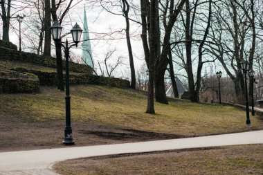 Sıcak ceketli ve kulaklıklı genç bir kadın soğuk bir günde çıplak ağaçlar ve klasik sokak lambalarıyla çevrili huzurlu bir şehir parkında yürüyor. Yüksek kalite fotoğraf