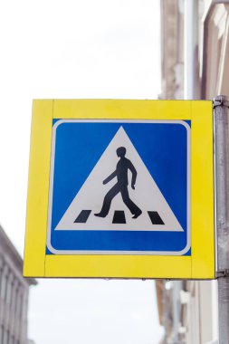 Şehir ortamında bir direğe monte edilmiş mavi ve sarı dizaynlı yaya geçidi tabelası yol güvenliğini ve trafik kurallarını sağlar. Yüksek kalite fotoğraf