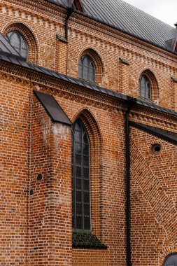 Tarihi tuğla bir kilisenin, kemerli camları ve bulutlu bir gökyüzünün altında metal bir çatısı olan, ortaçağ Avrupa mimarisinin detaylı bir görüntüsü. Yüksek kalite fotoğraf