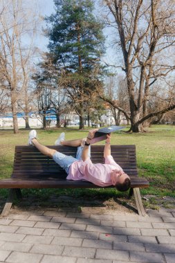 Odaklanmış bir öğrenci güneşli bir günde dışarıda dizüstü bilgisayarda çalışır ve parkta tek başına otururken notlar alır. Yüksek kalite fotoğraf