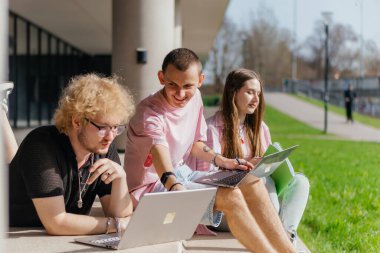 Güneşli bir günde bir grup öğrenci modern bir üniversite binasının önünde dizüstü bilgisayar çalışıyor ve kullanıyor. Yüksek kalite fotoğraf