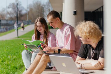 Güneşli bir günde bir grup öğrenci modern bir üniversite binasının önünde dizüstü bilgisayar çalışıyor ve kullanıyor. Yüksek kalite fotoğraf