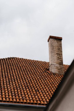 Bulutlu bir gökyüzünün altında geleneksel kırmızı kiremitli bir çatıda eski tuğla baca. Yüksek kalite fotoğraf
