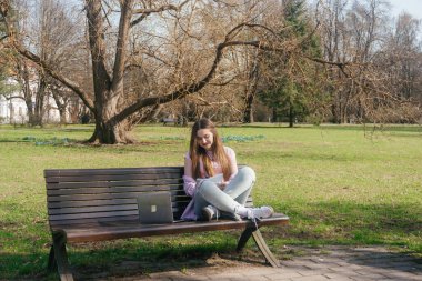 Öğrenci, güneşli bir bahar gününde dizüstü bilgisayarda çalışıyor ve dışarıda çalışıyor. Yüksek kalite fotoğraf