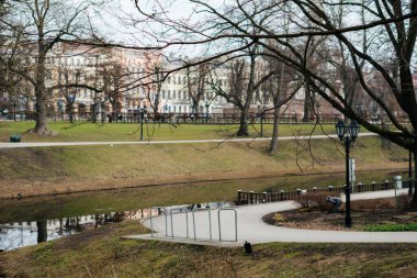 Sıcak ceketli ve kulaklıklı genç bir kadın soğuk bir günde çıplak ağaçlar ve klasik sokak lambalarıyla çevrili huzurlu bir şehir parkında yürüyor. Yüksek kalite fotoğraf